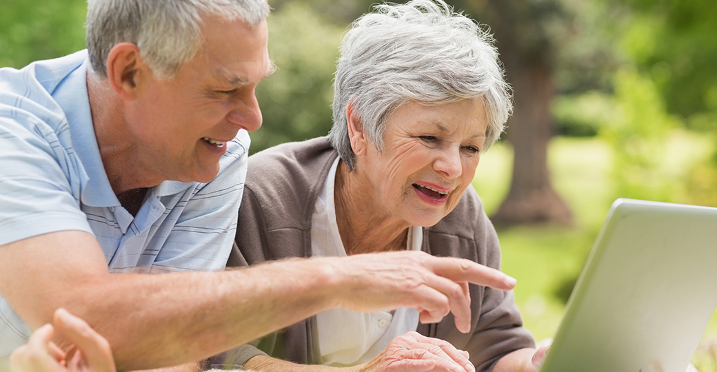 a senior man and woman outdoors reading from a laptop
